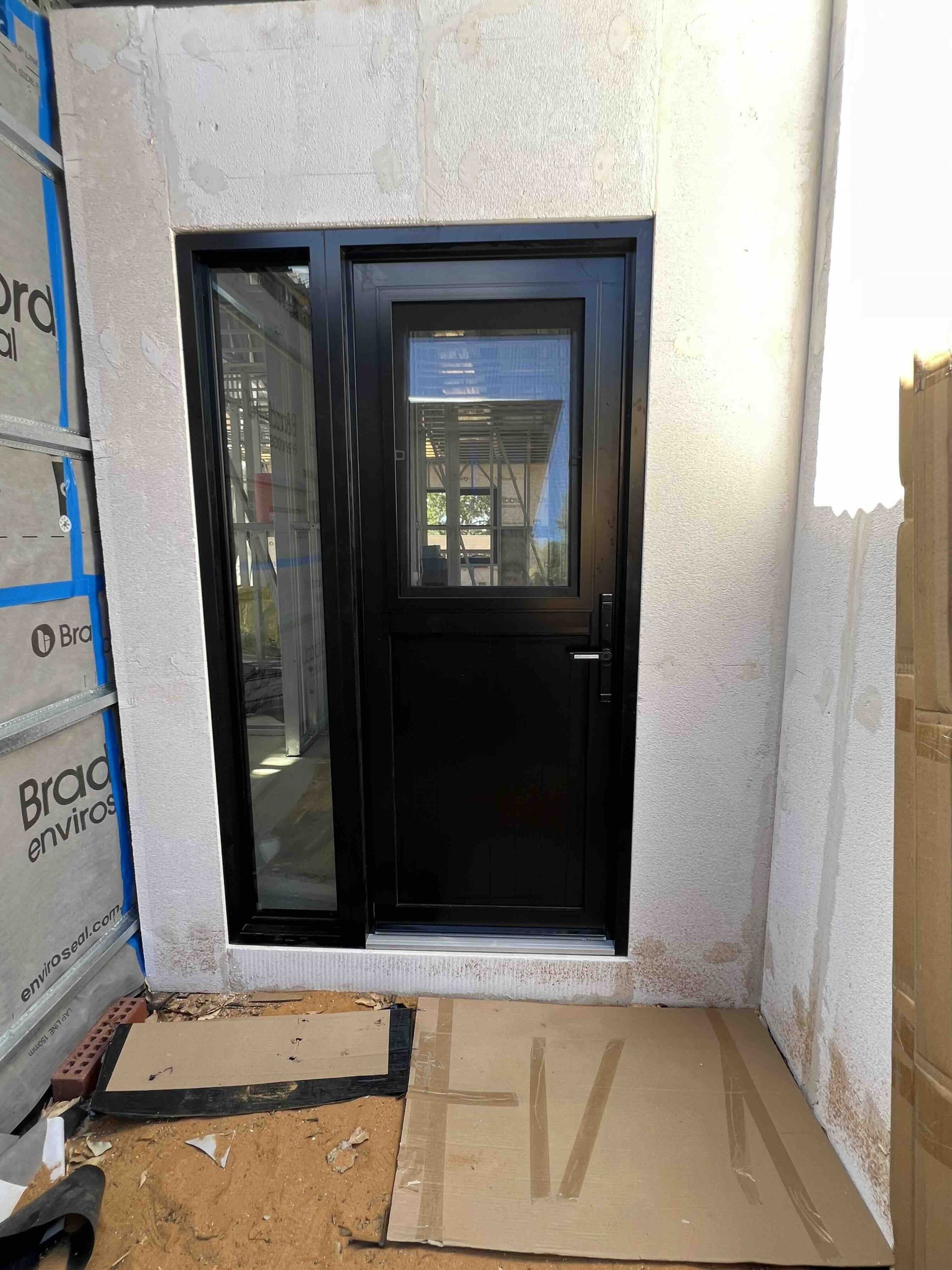 Black aluminium hinged entry door with narrow side light installed in Perth home by Penot Double Glazing, thermally broken frame with double glazing for energy efficiency and security.